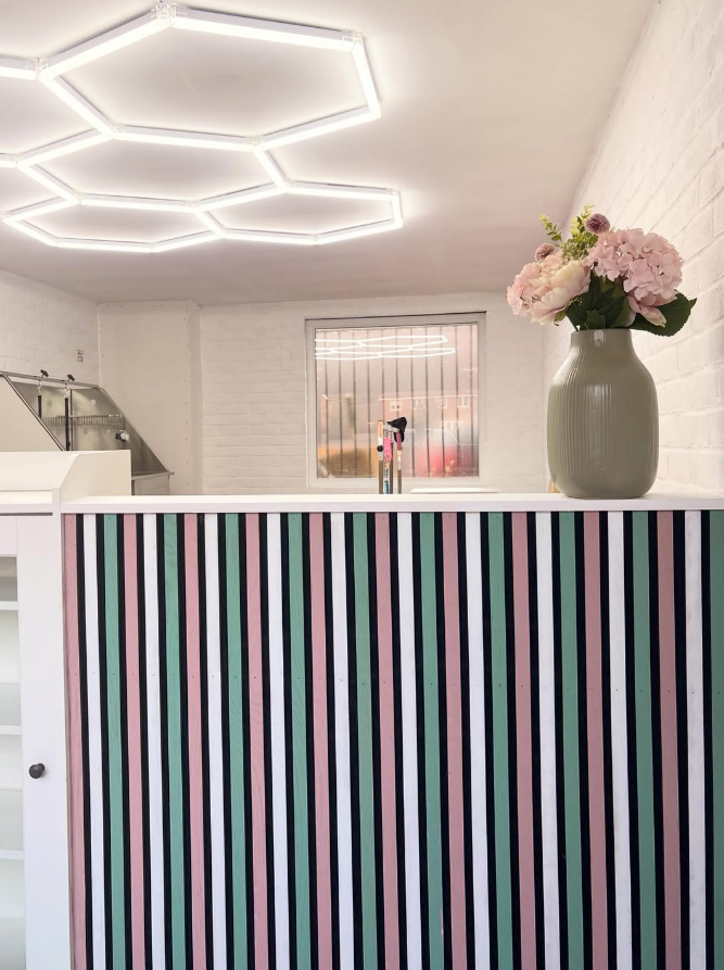 Geometric hexagon lighting above the Ivory Tails grooming studio, with the sage and blush striped reception counter and fresh pink hydrangeas